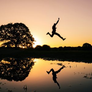 silhouette photo of man jumping on body of water during golden hour